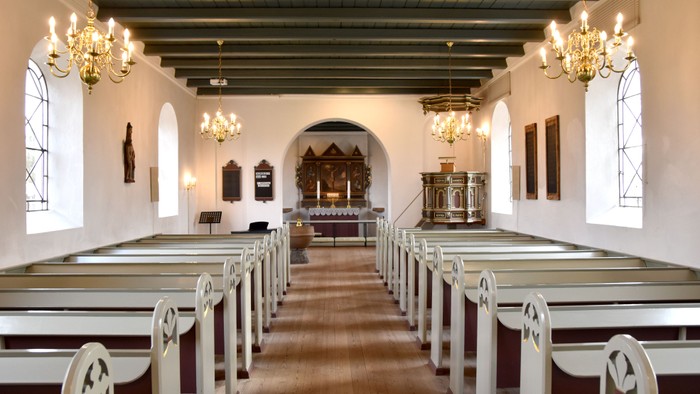 Indre del af kirke med hvidt indretning og hængende lygter
