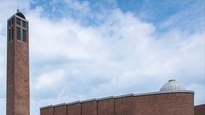 Das Bild zeigt einen Ziegelbau mit hohem Turm und gewölbter Struktur unter blauem Himmel.