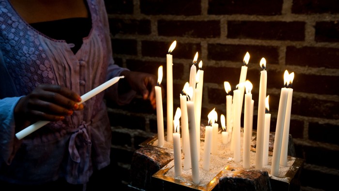 En person lader lys på tallitinder foran mursten.