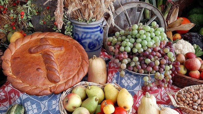 Verschiedene Obst- und Gemüsesorten, arrangiert auf einem Tisch mit einem Laib Brot und einem Glas.