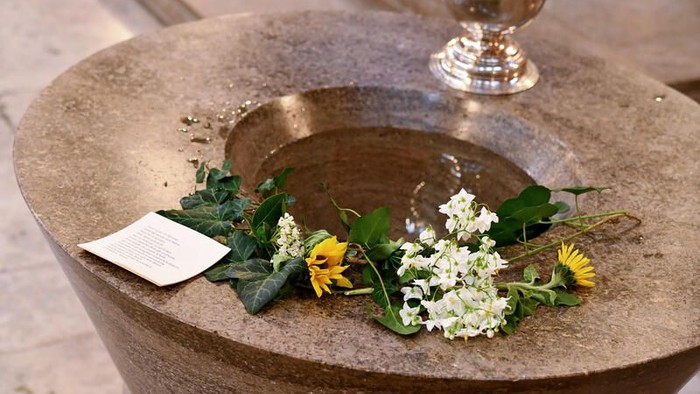 Ein steinernes Brunnenbecken, gefüllt mit Wasser, umgeben von Blumen und einer kleinen Karte.