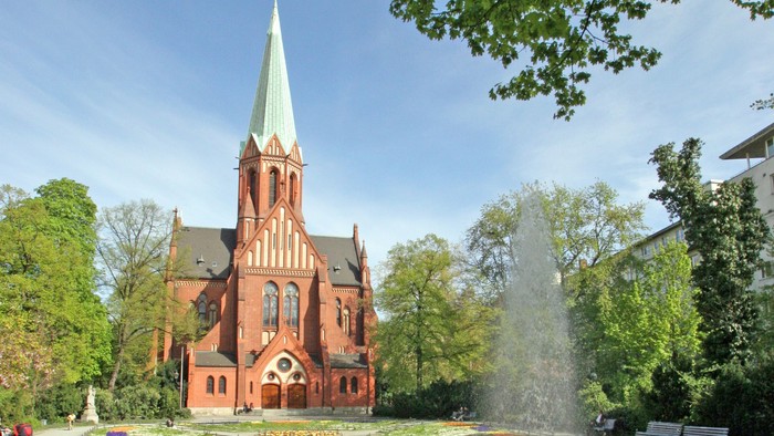 Ein rotes Kirche mit hohem Turm und ein Brunnen im Vordergrund