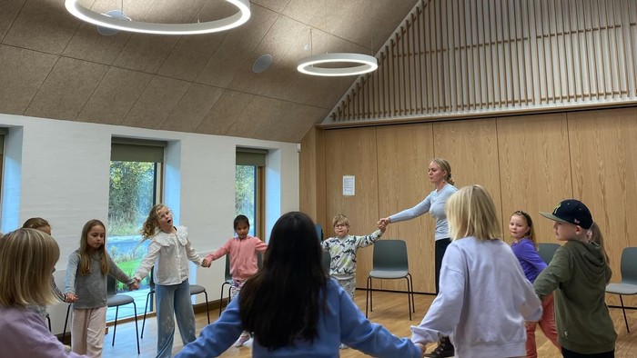 En gruppe af børn holder hånd i en hall med høje tak og store vinduer