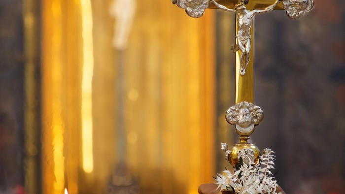 Eleganter goldener Kruzifix mit Kerze und Blumenschmuck in einer heiligen, beleuchteten Umgebung.