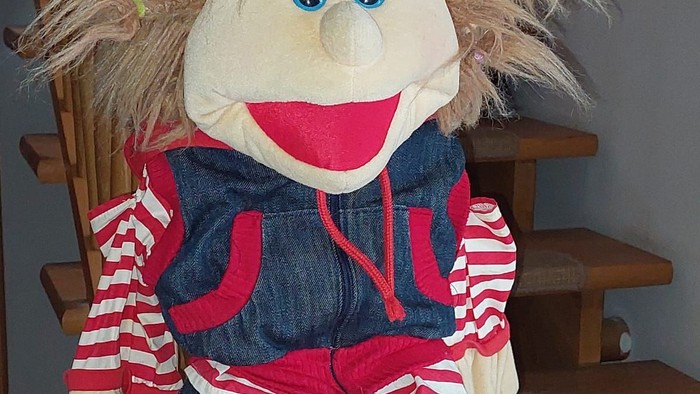 Puppenfigur mit wildem Haar sitzt auf einem Stuhl.