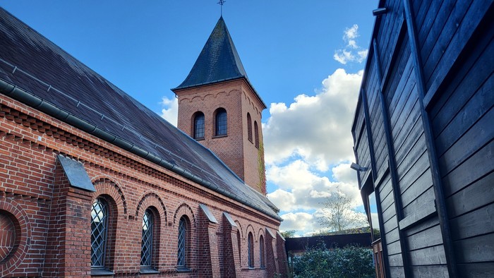 En rød murstenskirke med tårn og bjælker, set fra siden
