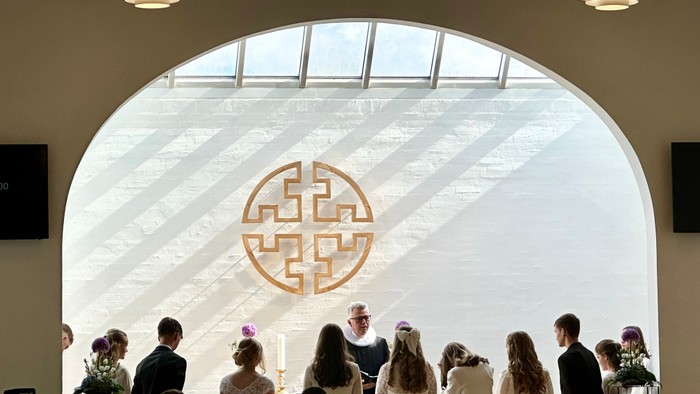 En bryllupsceremoni finder sted i en lys og rummelig sal med bogstaver på væggen.