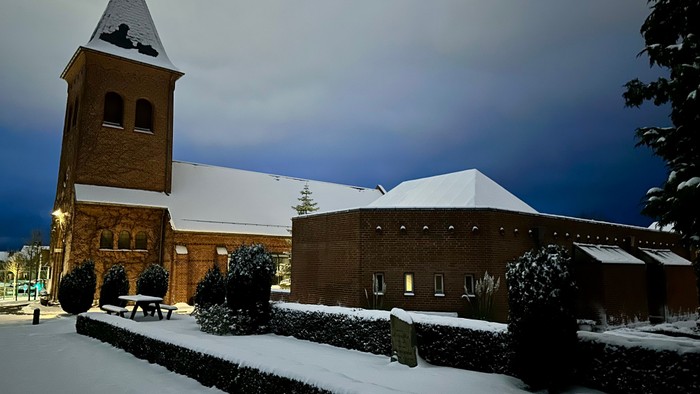 En rolig sneklædt aften ved en murstenskirke med et højt klokketårn og en tilstødende bygning.