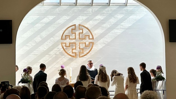 En bryllupsceremoni finder sted i en lys og rummelig sal med bogstaver på væggen.