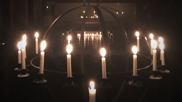 En mørk rom med mange lysende lysekænder og en stor kugle i midten.