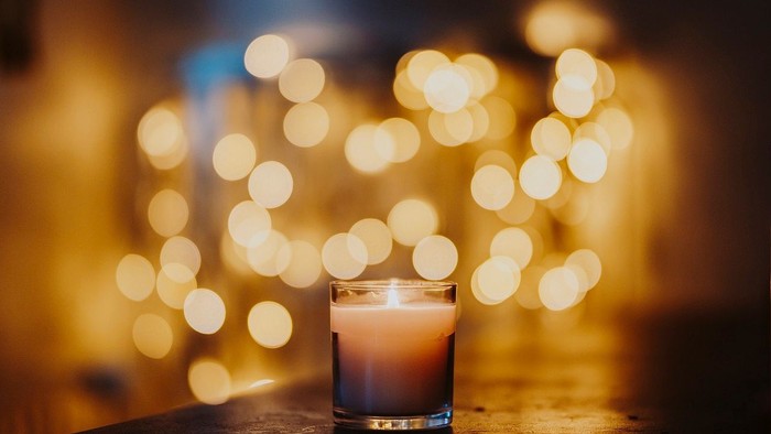 Eine brennende Kerze steht auf einem Tisch vor einem Hintergrund aus weihnachtlichen Lichtern.