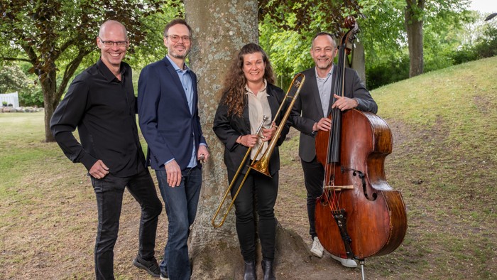 Fire musikerer står sammen med deres instrumenter i en park