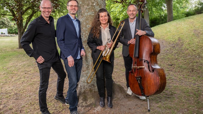Fire musikerer står sammen med deres instrumenter i en park