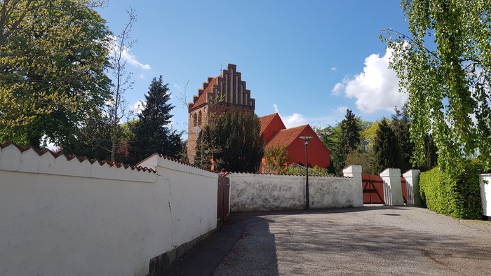 En hvid mur med en indgang til en trækirke med røde tag.