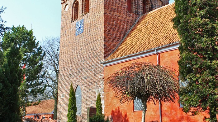 Røde murstensbygning med klokketårn og gule tegltag.