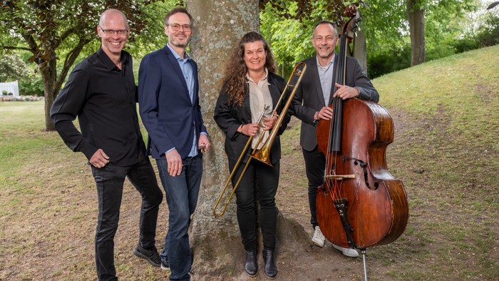 Fire musikerer står sammen med deres instrumenter i en park