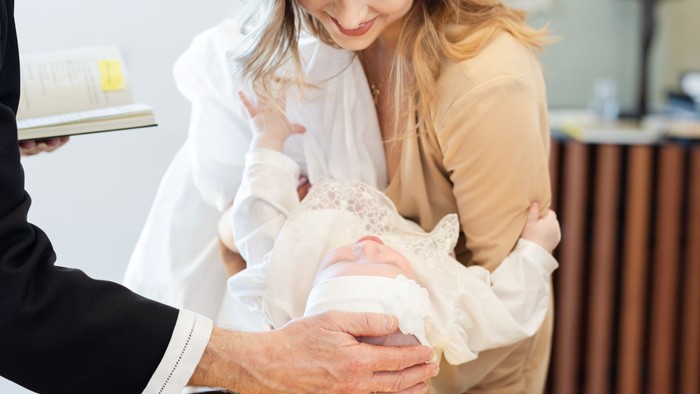 En dåbsceremoni, hvor en præst hælder vand over et spædbarn, som holdes af dets forældre.