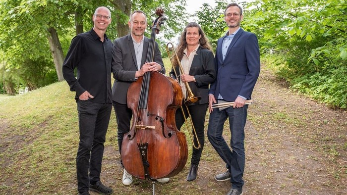 Fire mænd står sammen med en cello i en park