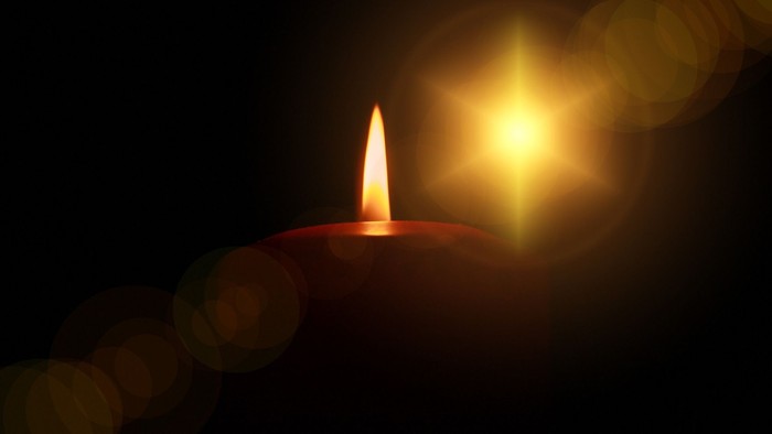 Eine brennende Kerze vor dunklem Hintergrund mit hellem Lichteffekt.