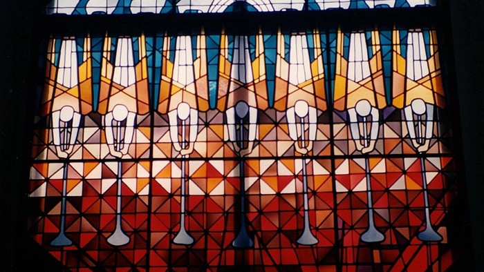 Buntes Kirchenfenster mit geometrischen Mustern und Kerzen.