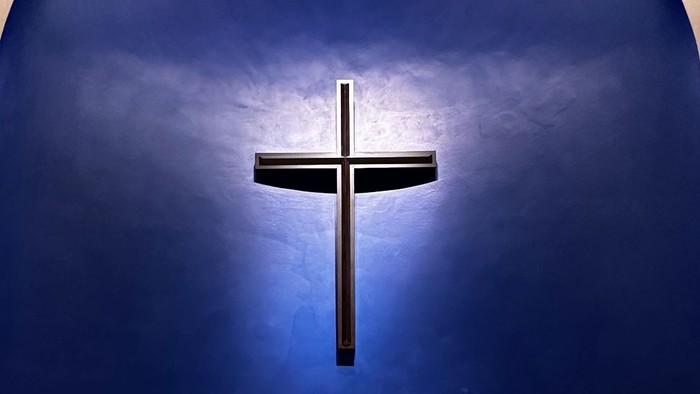 Ein weißer Kerzenleuchter steht vor einem großen Holzkreuz an einer blauen Kirchenwand