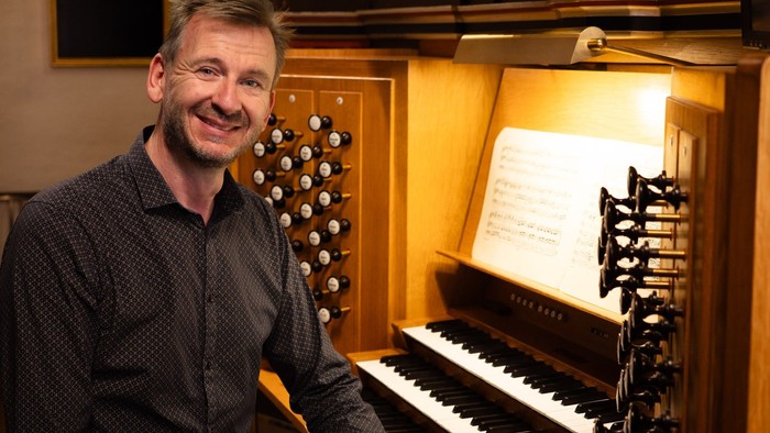 Mand sitter ved et orgel og smiler til kameraet