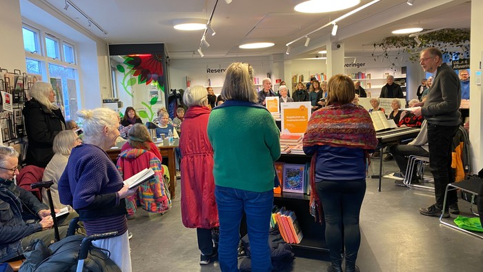Mange mennesker står op og synger på offentligt bibliotek