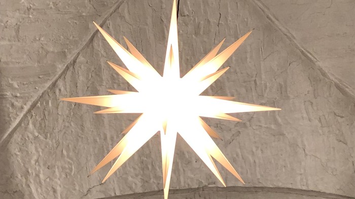 Ein großer, hell leuchtender Stern hängt von der Decke einer Kirche.