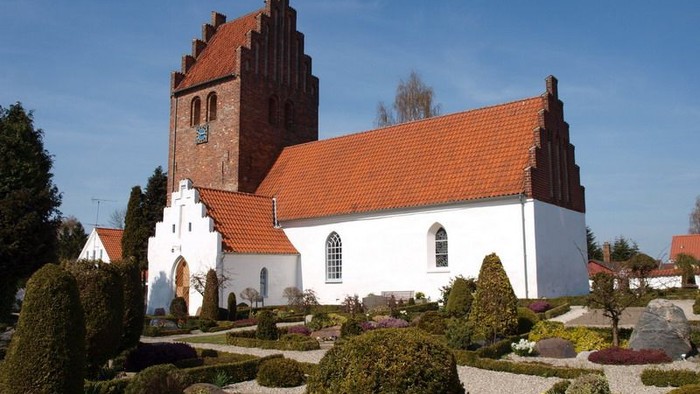 En hvid kirke med røde tag og tårn i en parkagtig have