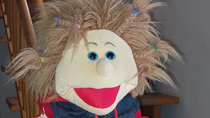 Puppenfigur mit wildem Haar sitzt auf einem Stuhl.