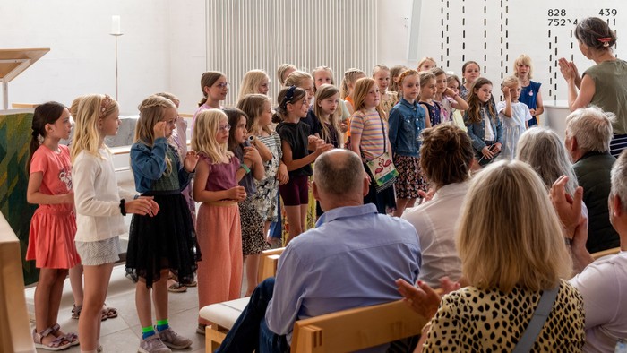 En gruppe mennesker, herunder børn og voksne, samlet i en kirke til en fælles aktivitet eller ceremoni.