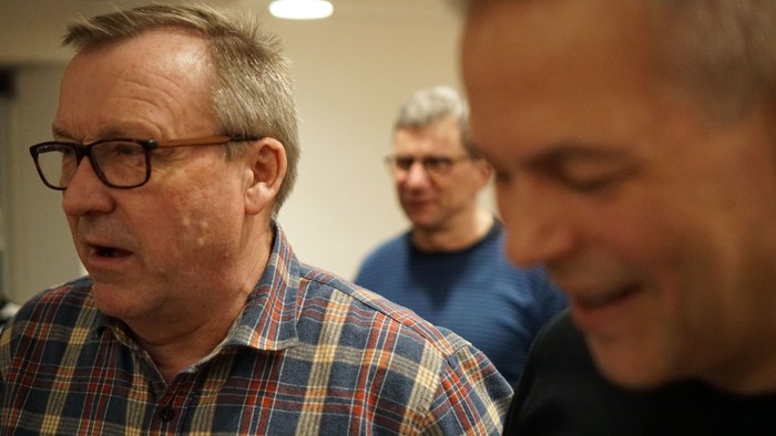 To mænd står og snakker i et rum.