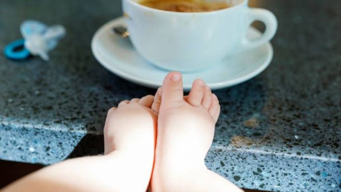 Et barn sitter med benene på bordet ved en kaffe.