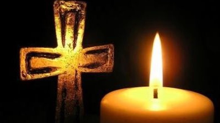 En lysende lyse med en tændt lyse og en trækors i mørke omgivelser