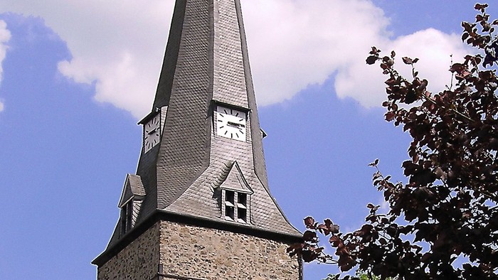 Ein hoher Kirchturm ragt in den klaren blauen Himmel.