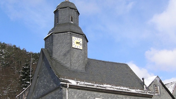Graues Kirchgebäude mit Uhrturm und Schnee auf dem Dach