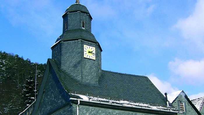 Kirchengebäude mit Uhrturm und Schieferfassade
