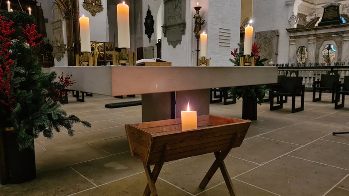 In der Kirche steht ein hölzernes Taufbecken mit einer brennenden Kerze, umgeben von Weihnachtsdekorationen.