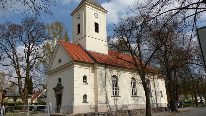 Kleine weiße Kirche mit rotem Dach und Turm in parkähnlicher Umgebung