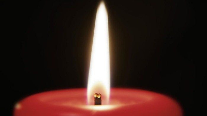 Eine einzelne rote Kerze brennt hell gegen einen dunklen Hintergrund.