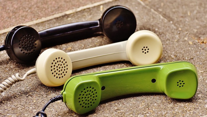 Drei Telefonhörer in Schwarz, Weiß und Grün liegen auf dem Boden