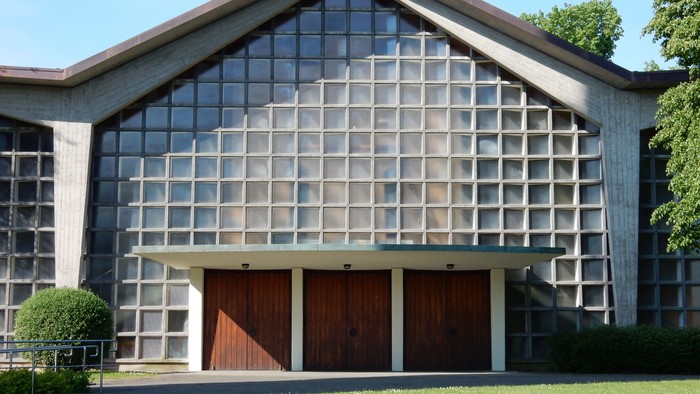 Moderne Kirche mit großem Glasfenster und Holztüren vor grünem Hintergrund