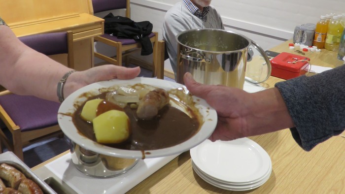 En person serverer sig selv fra en buffet med mad.