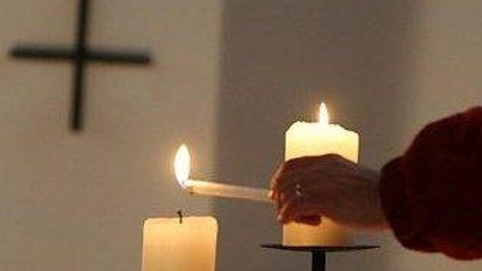 En hånd tænder en lysestage foran et lyset i en kirke.
