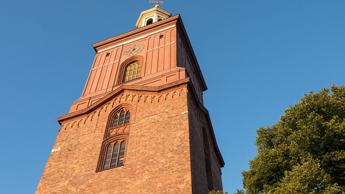 Der hohe Ziegelbau mit Uhr und goldenem Dachtürmchen ragt in den klaren blauen Himmel