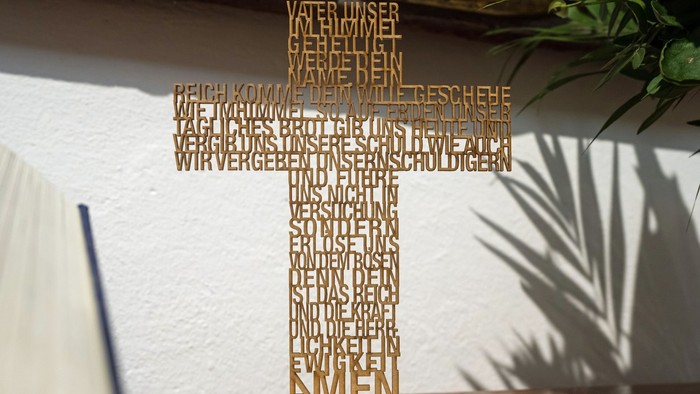 Ein hölzernes Kreuz mit eingraviertem Text steht auf einem Tisch.