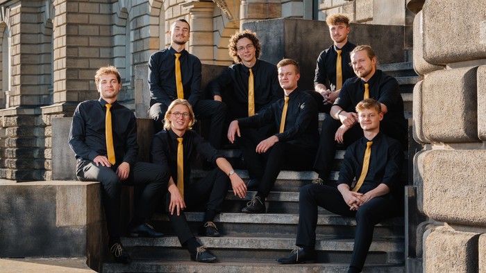 Ein Männerchor posiert in Anzügen auf Treppenstufen.