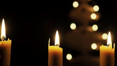 Tre lysende lysekænder foran en lyssvag juletræ.