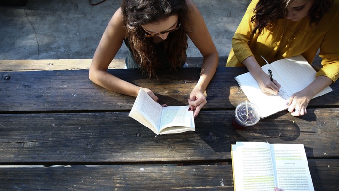 Zwei Frauen sitzen auf einer Holzbank und lesen Bücher.