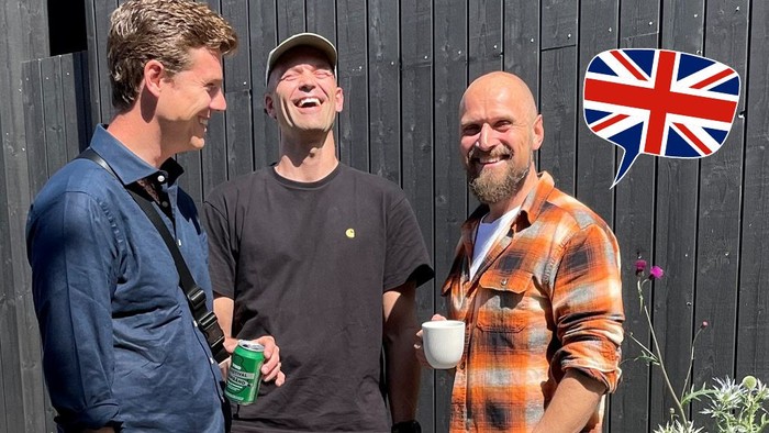 Tre mænd står sammen og smiler, en af dem holder en grøn flaske.